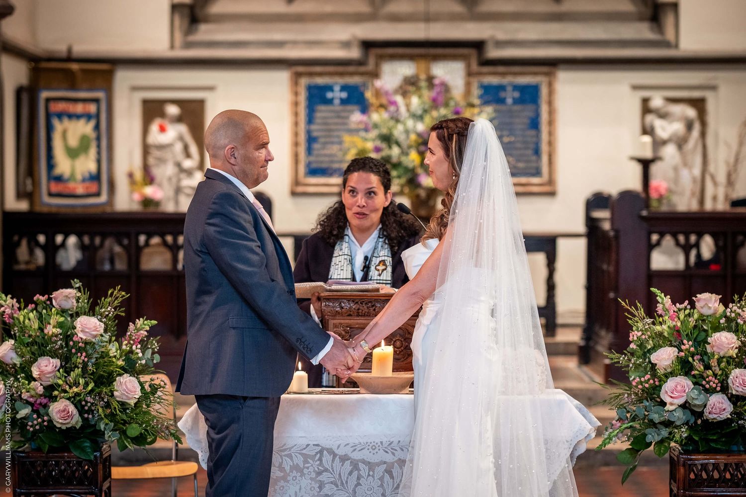 A tender moment at the altar during a wedding ceremony in a church adorned with pink floral arrangements.