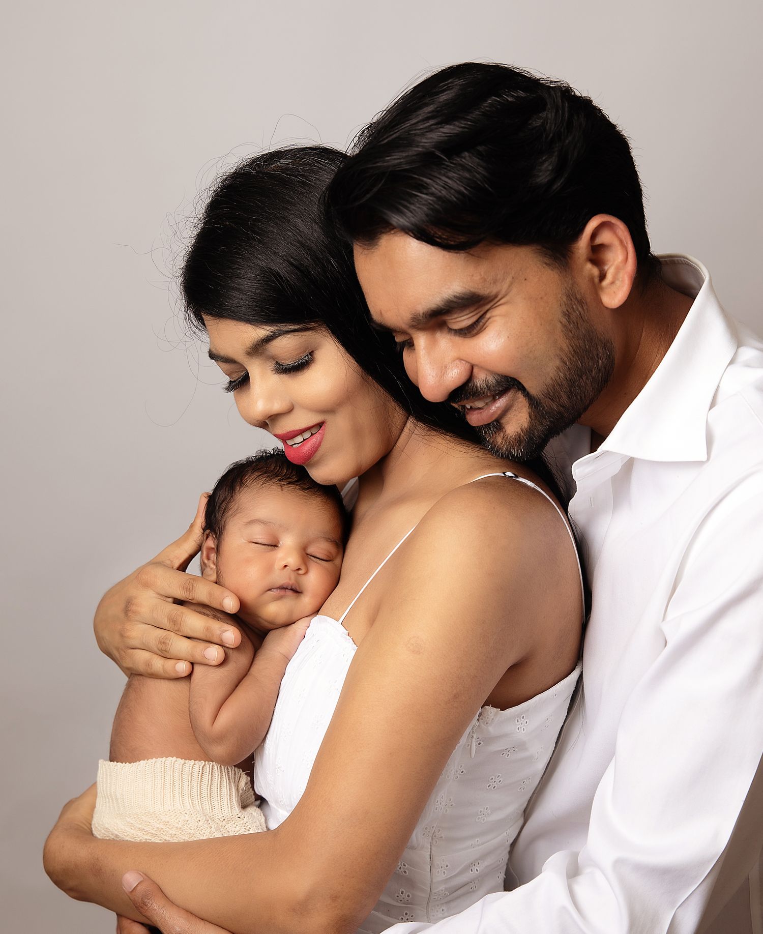 A loving couple holds their newborn baby in a heartfelt studio portrait against a neutral background. During a photoshoot in Bexley