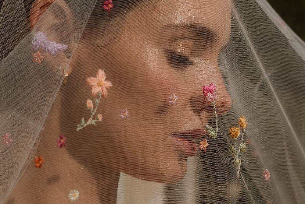 Close-up profile view of someone wearing sheer veil with delicate colorful floral appliques and closed eyes.
