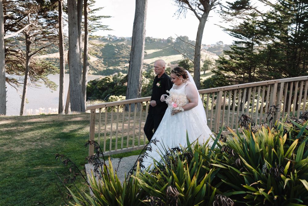 Wedding couple walking along a wooden deck pathway overlooking the ocean.