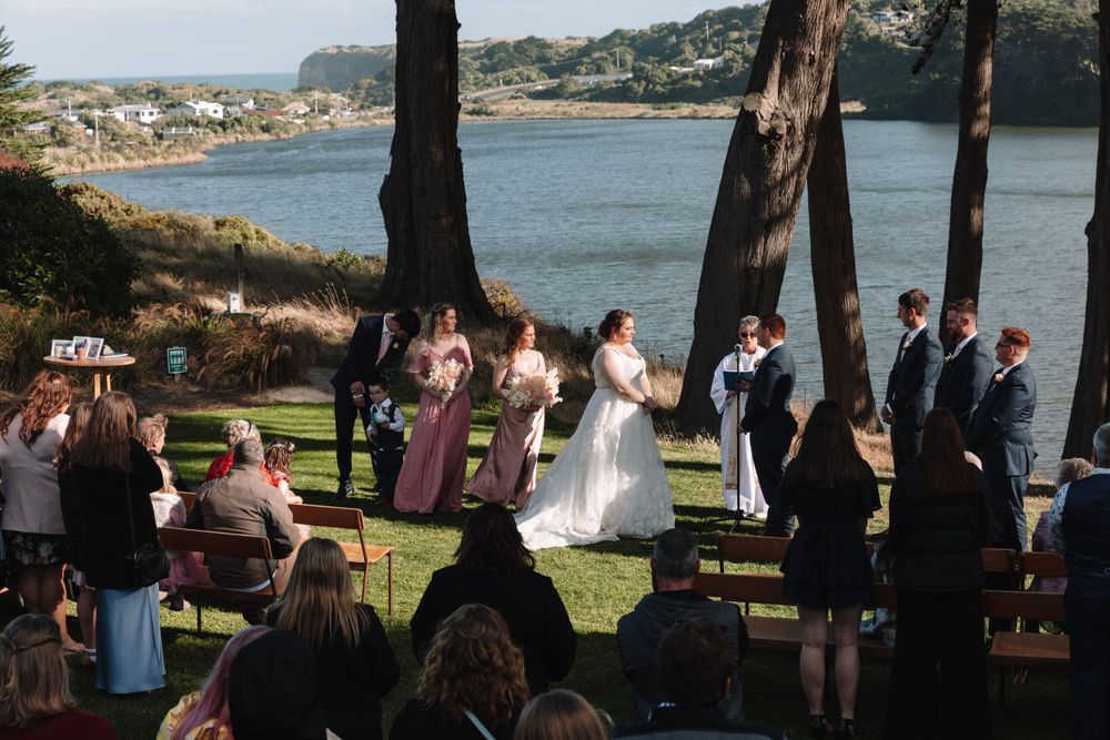 Wedding ceremony taking place on a cliff overlooking a coastal bay with guests in attendance.