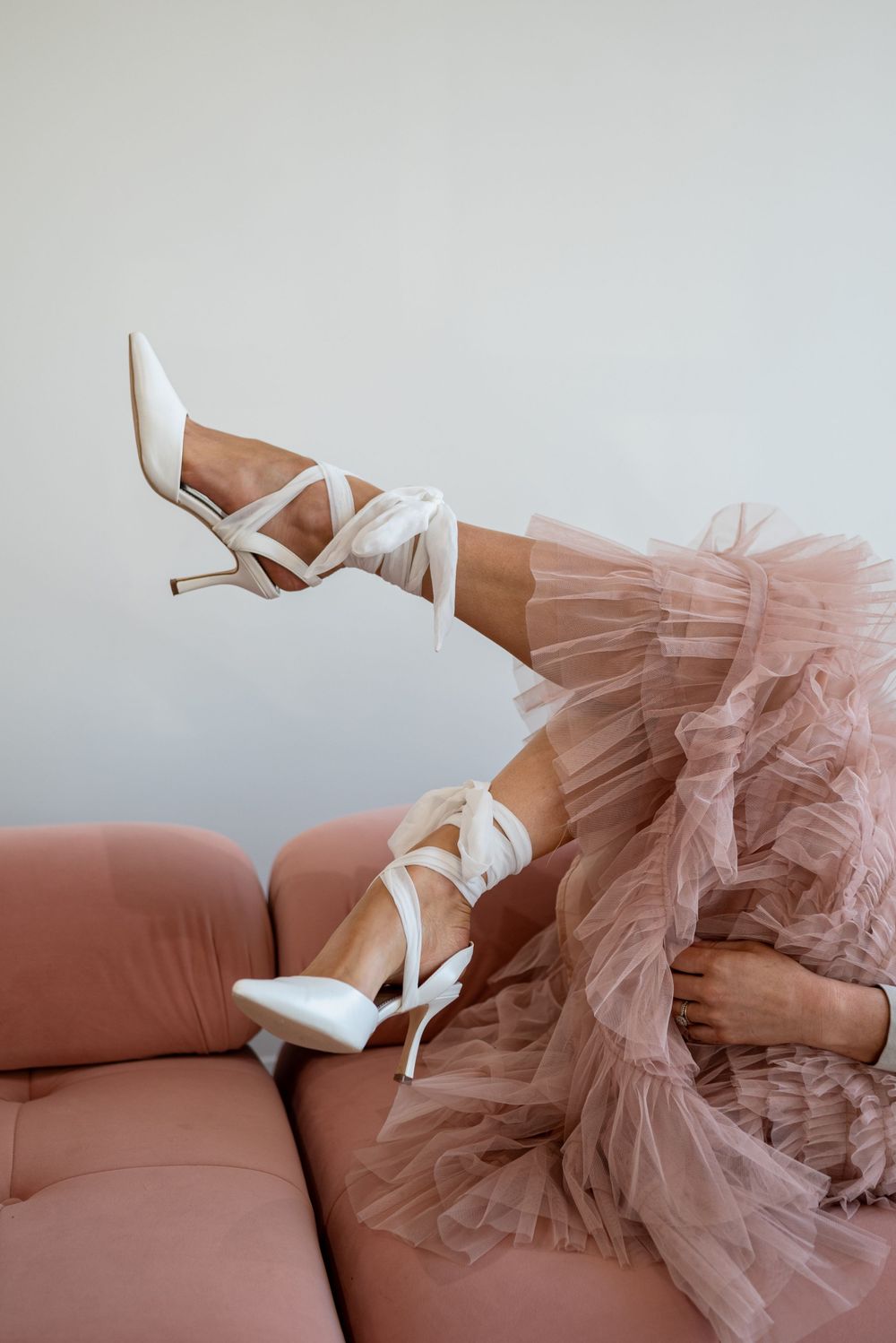 White strappy heels and pink tulle skirt draped over salmon colored couch.