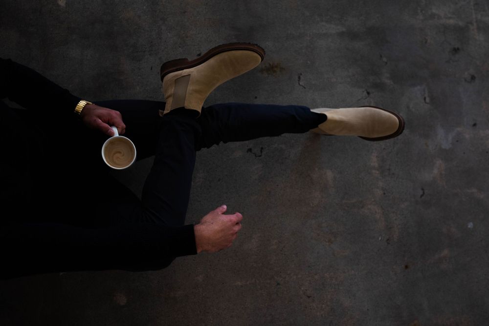 Artistic overhead shot of person balancing coffee cup while laying on dark floor.