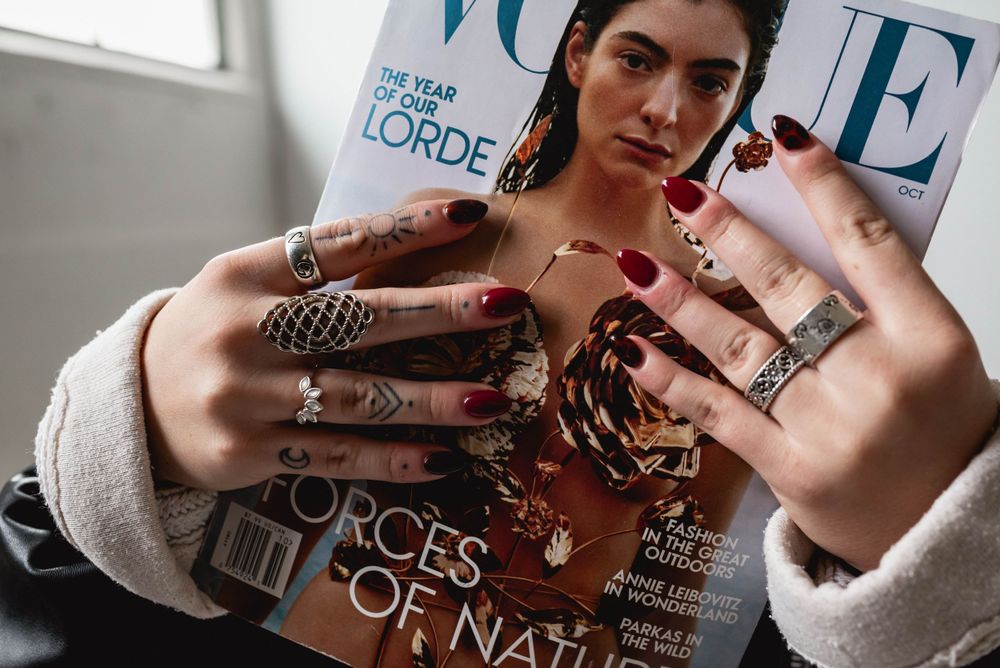 Close up of hands with rings and red nails holding fashion magazine cover.