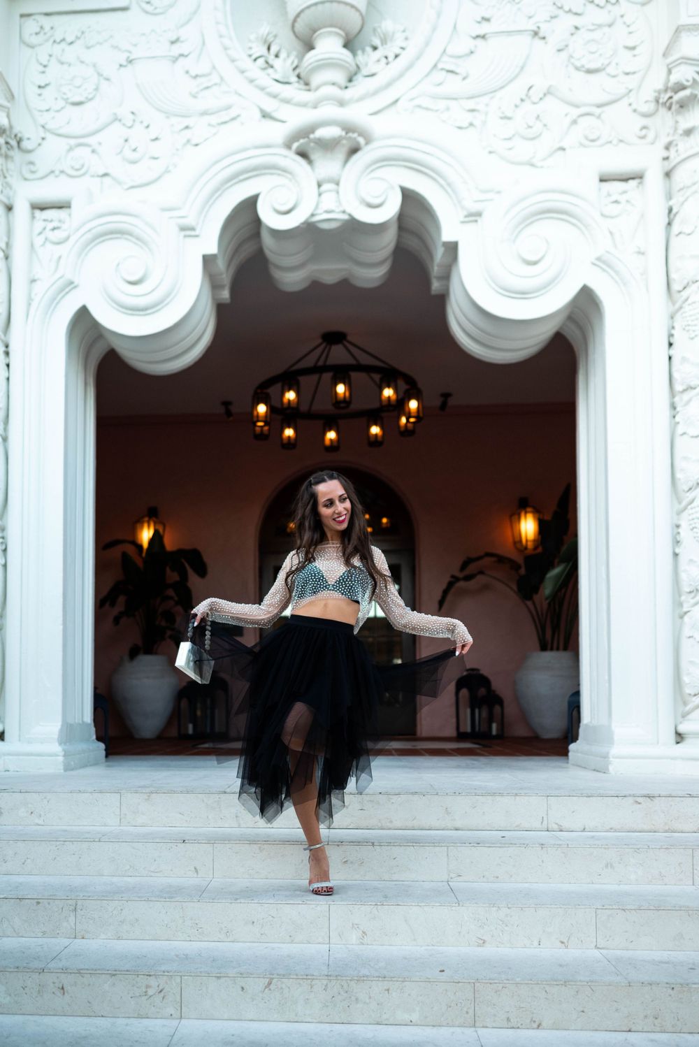 Dancer in two-piece outfit posing on white ornate steps of grand building entrance.