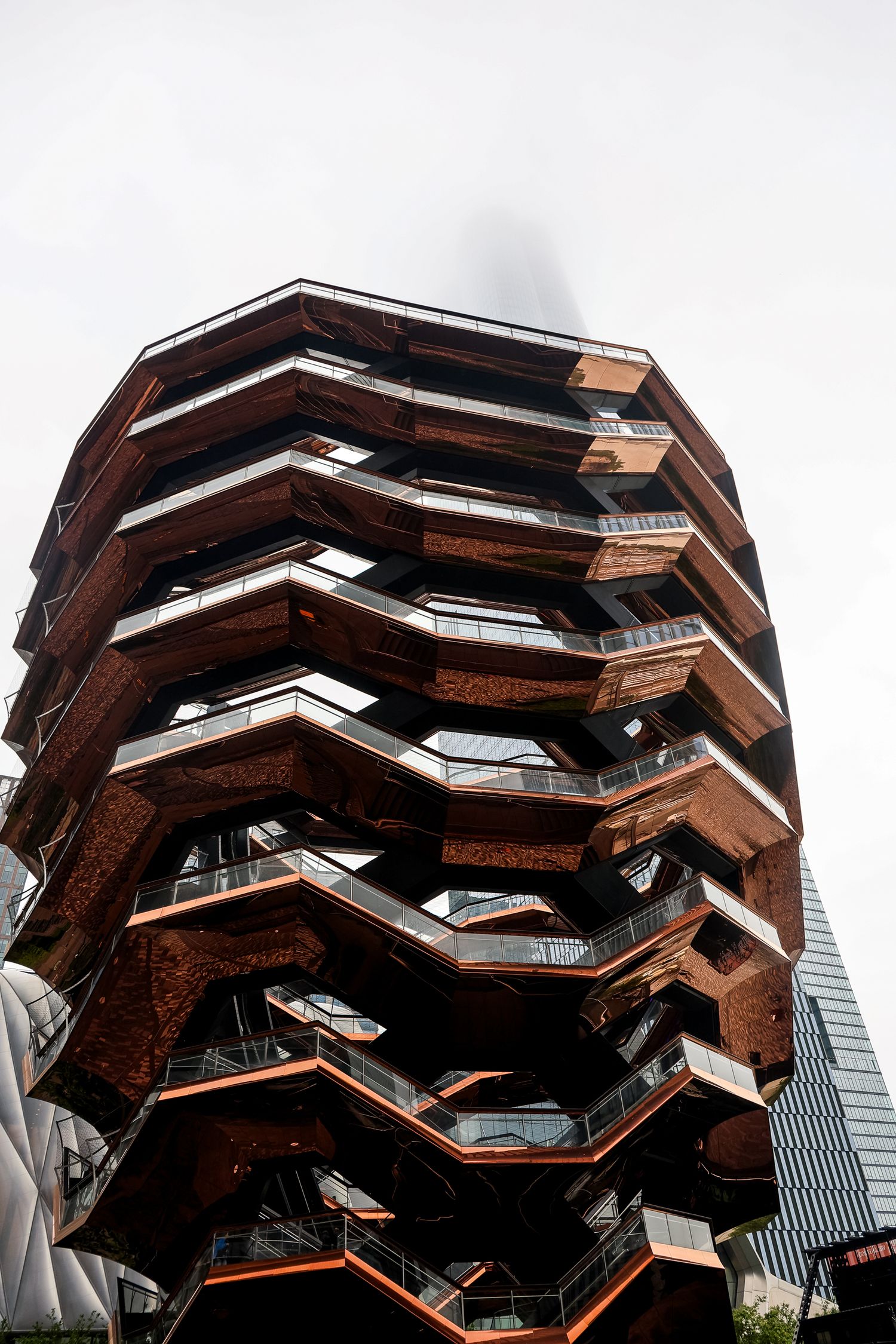 The Vessel at Hudson Yards features a distinctive spiral staircase design with copper-colored geometric patterns against a city backdrop.