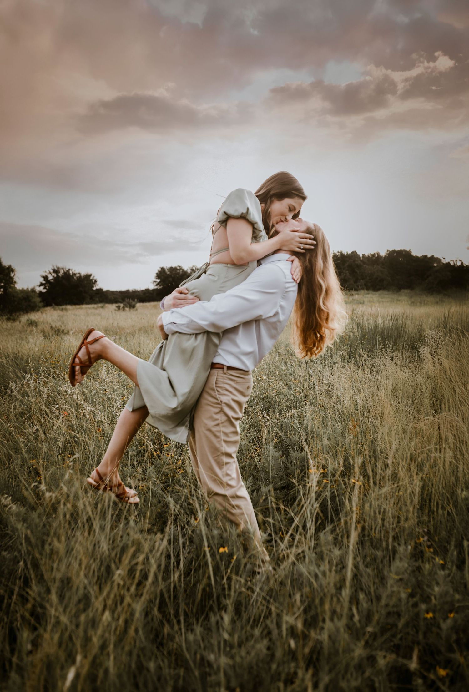 Groom-to-be lifting his fiancée playfully in a golden field