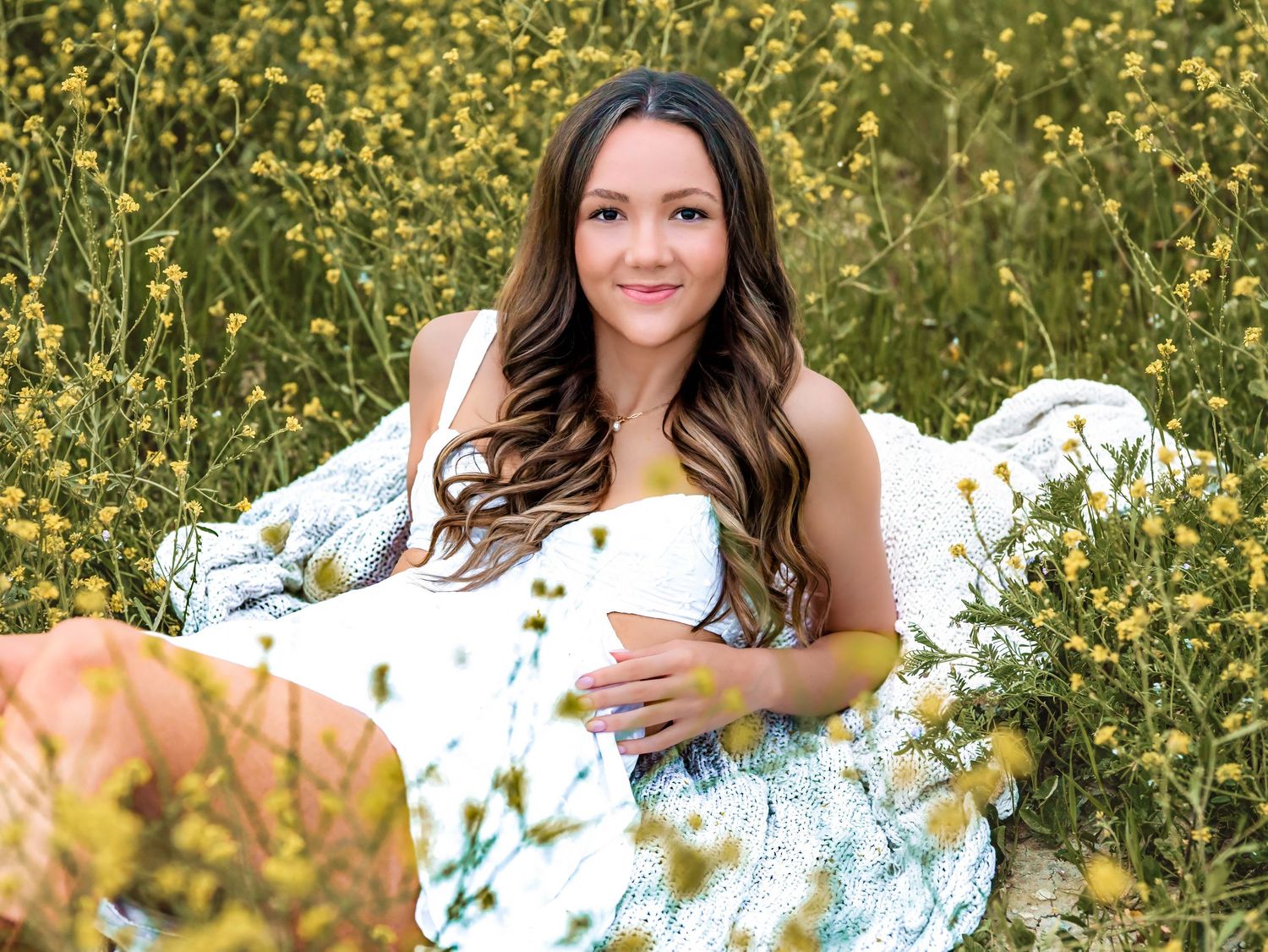 A person in a white dress lies among blooming yellow wildflowers on a sunny day creating a dreamy outdoor portrait.