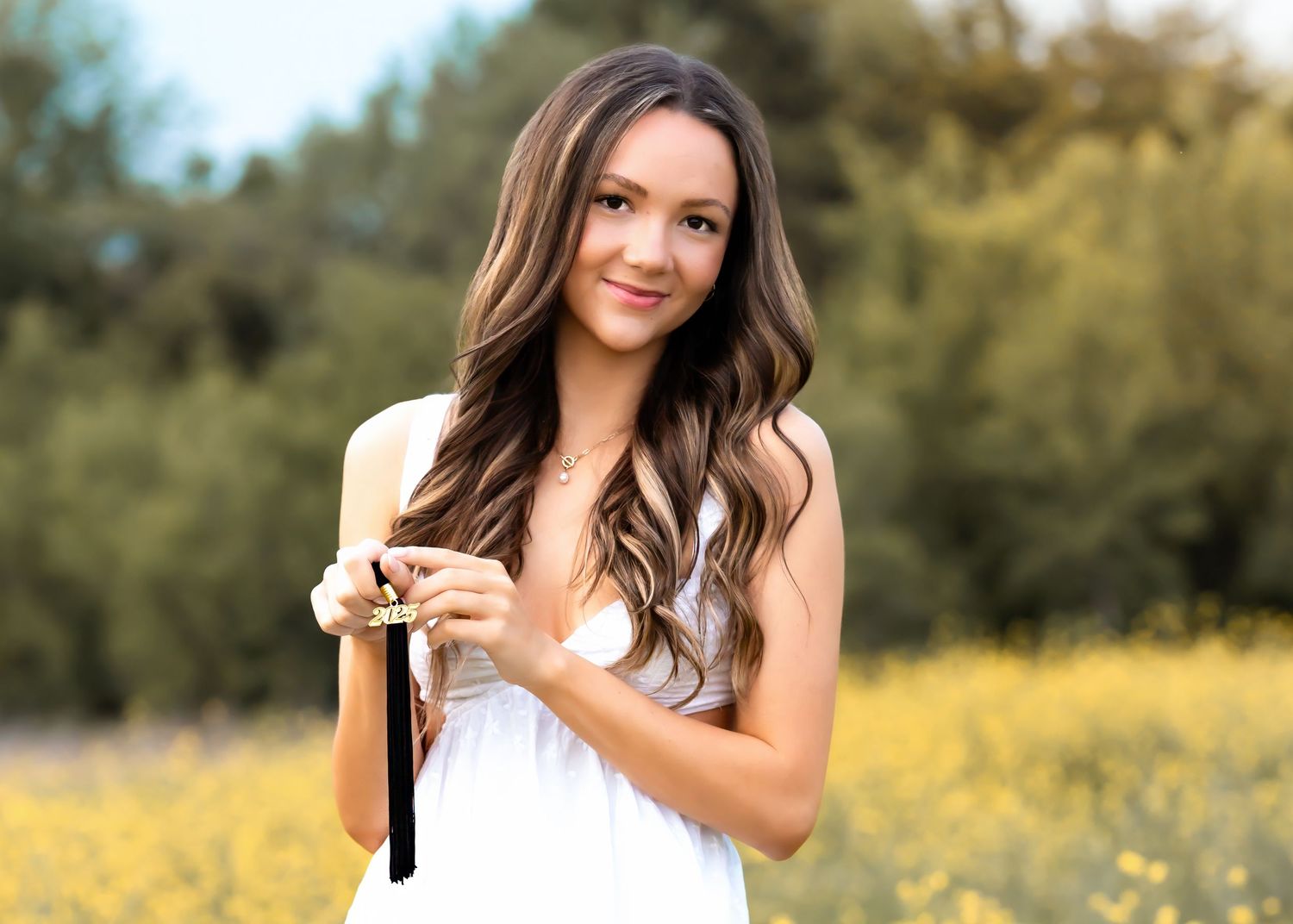 A young woman in a white dress holds a vintage camera while standing in a sunny meadow with blurred trees behind her.