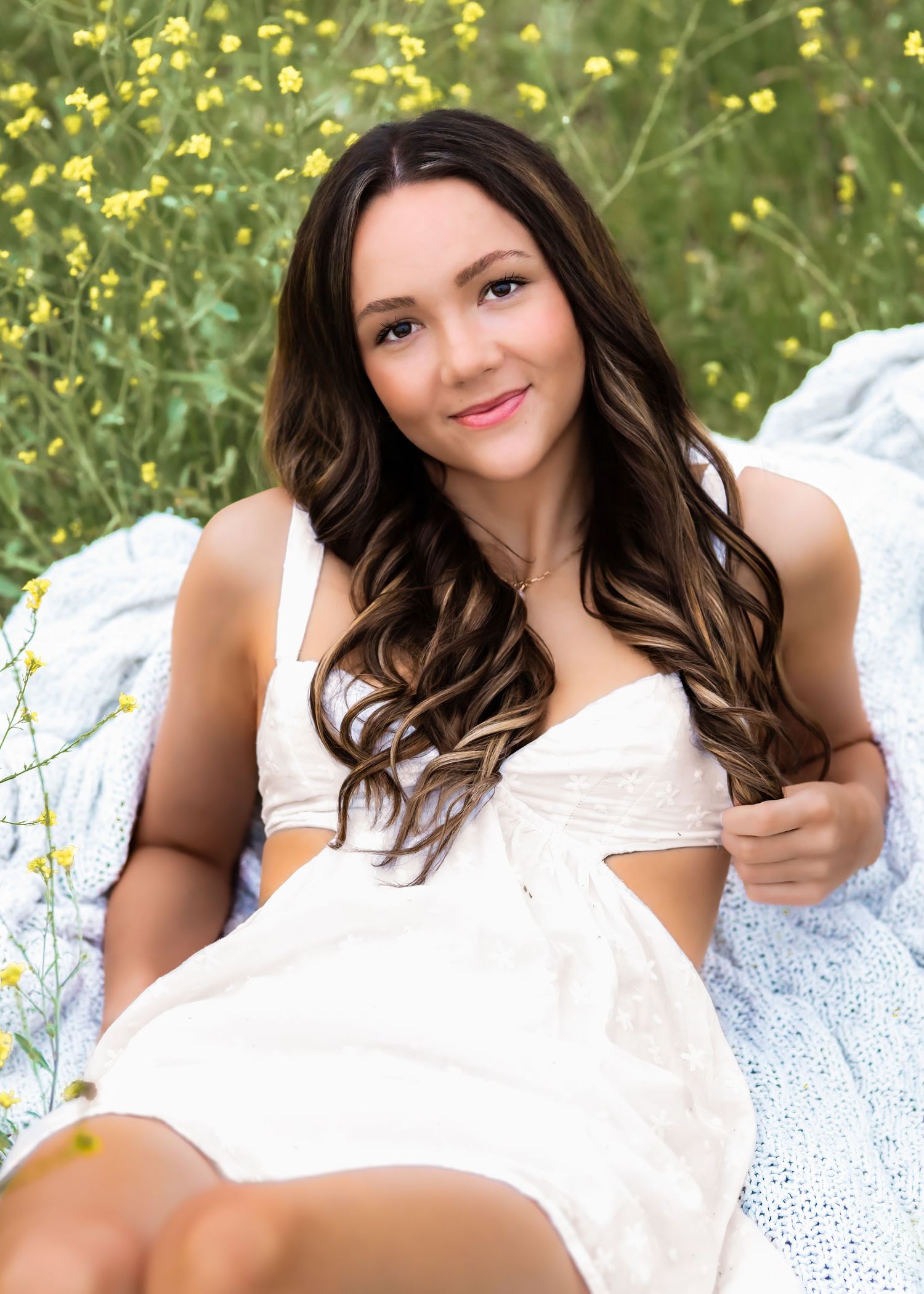 Someone in a white dress relaxes on a blanket outdoors among yellow wildflowers on a sunny summer day.