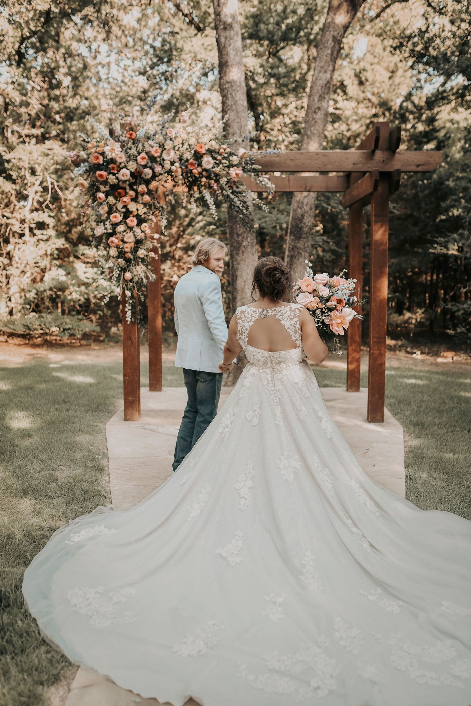 Bride leaning into groom under a wooden arch covered in roses and greenery