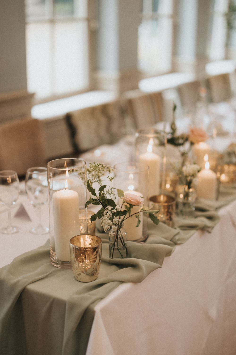 Elegant wedding table setting with sage green runner, white candles, and delicate floral arrangements at Washingborough Hall.