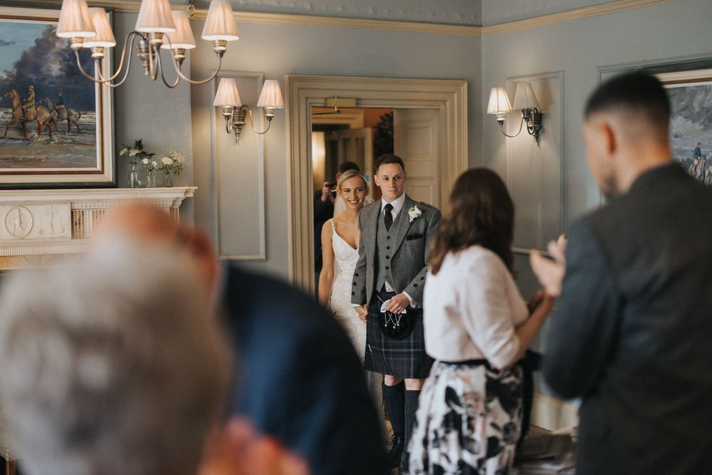 Wedding guests mingle and socialise in an elegant ballroom with white decor and chandeliers at Washingborough Hall - by Grimsby photographer