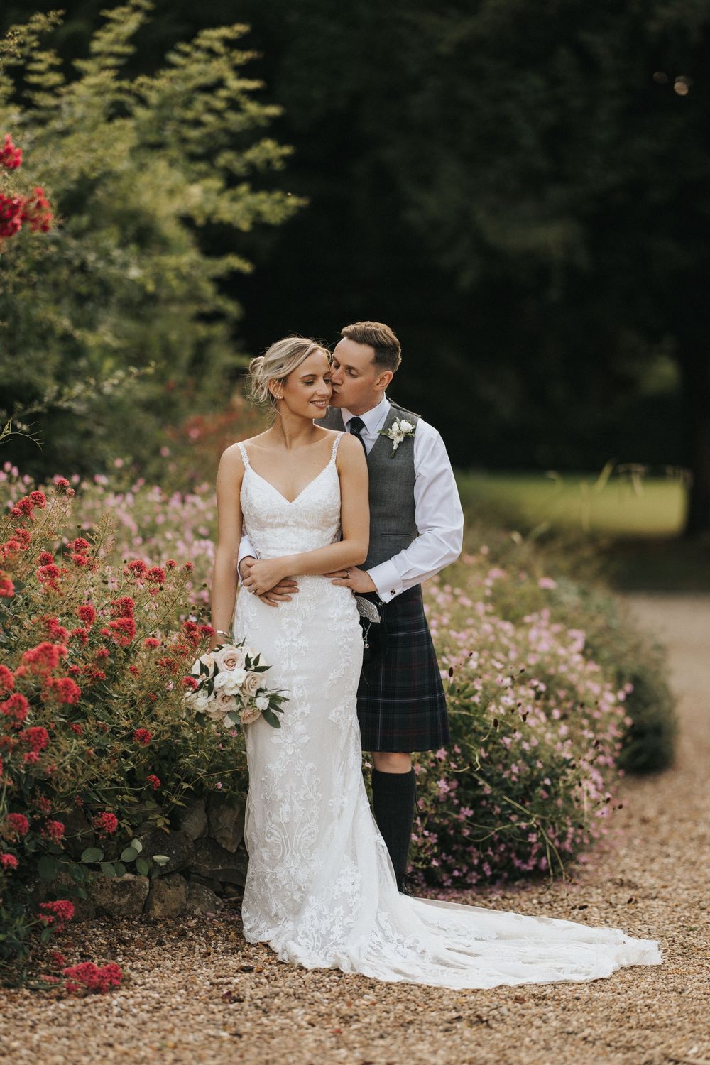 A romantic wedding couple embraces in a garden setting with beautiful red flowers at Washingborough Hall - taken by Grimsby photographer.