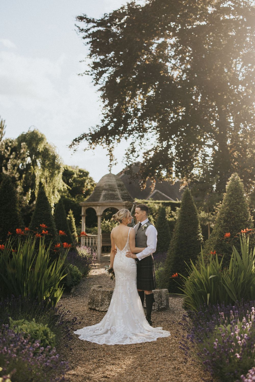A couple in wedding attire stands by a gazebo in a lush garden with vibrant flowers at Washingborough Hall - taken by Grimsby photographer.