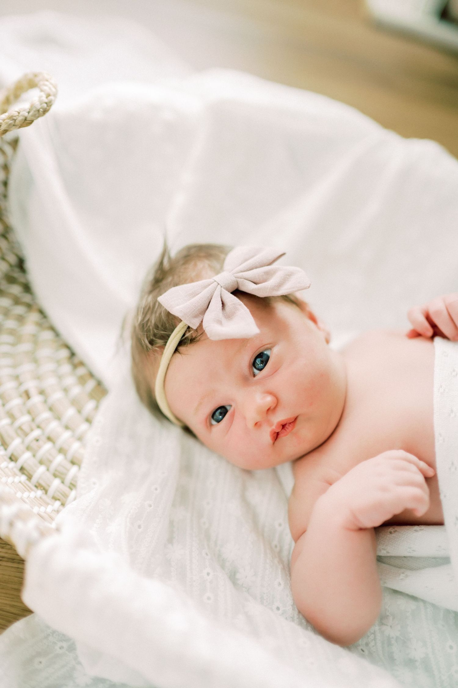 A baby wrapped in soft white blankets lies peacefully on a textured knit surface in a series of gentle poses.
