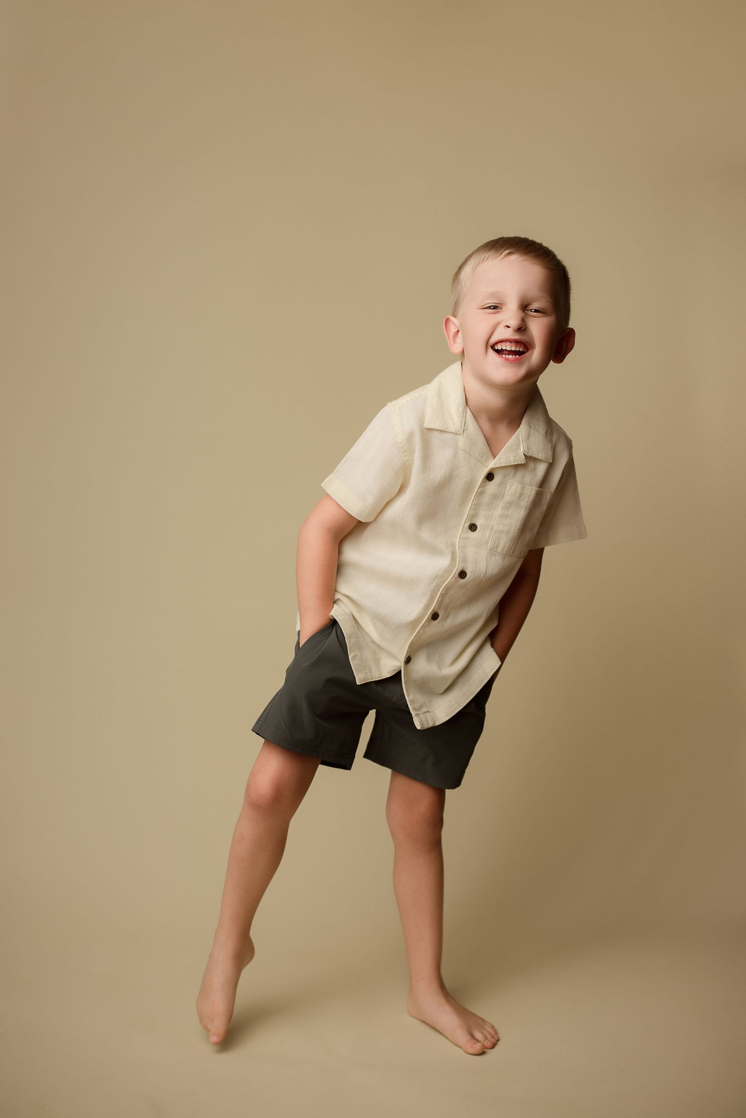 A sequence of photos showing a child in cream colored shirt and dark shorts making playful poses on a neutral backdrop.