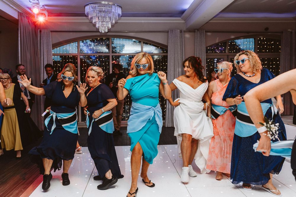 Wedding reception dance party with guests in colorful dresses dancing energetically.
