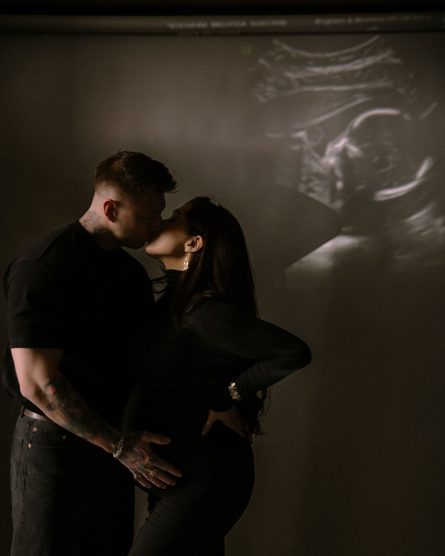 A couple embraces in darkness while their ultrasound scan is projected on the wall beside them.
