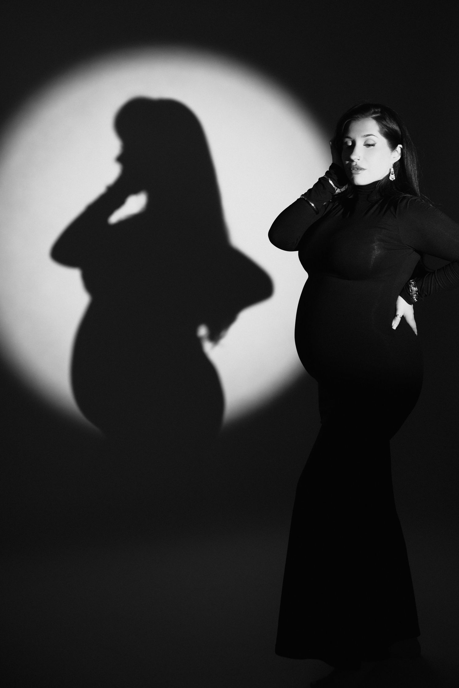 Artistic black and white photo of a person in a long dress with dramatic shadow cast on white wall behind them.