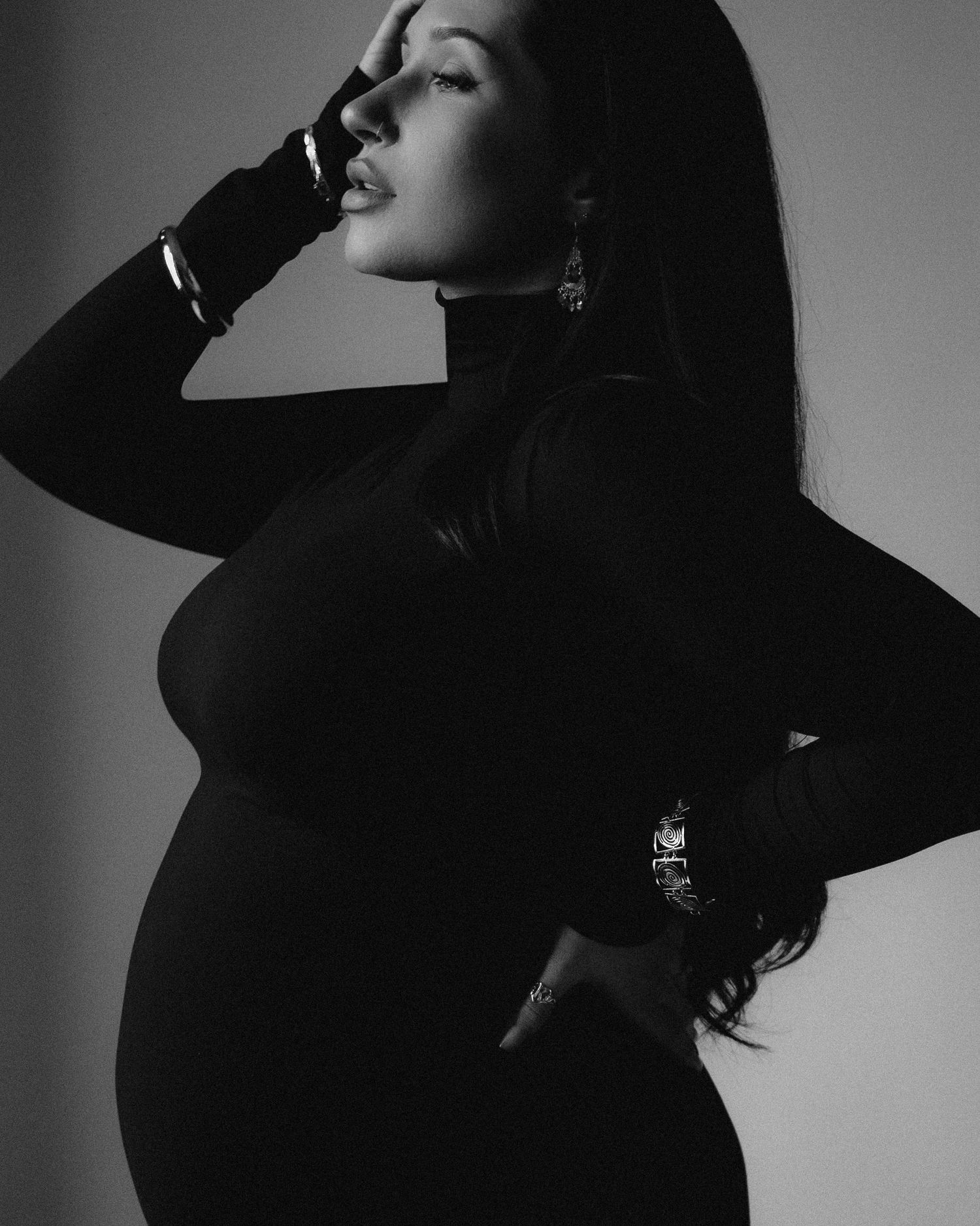 Dramatic black and white fashion portrait of a glamorous silhouette in profile wearing all black against moody lighting.