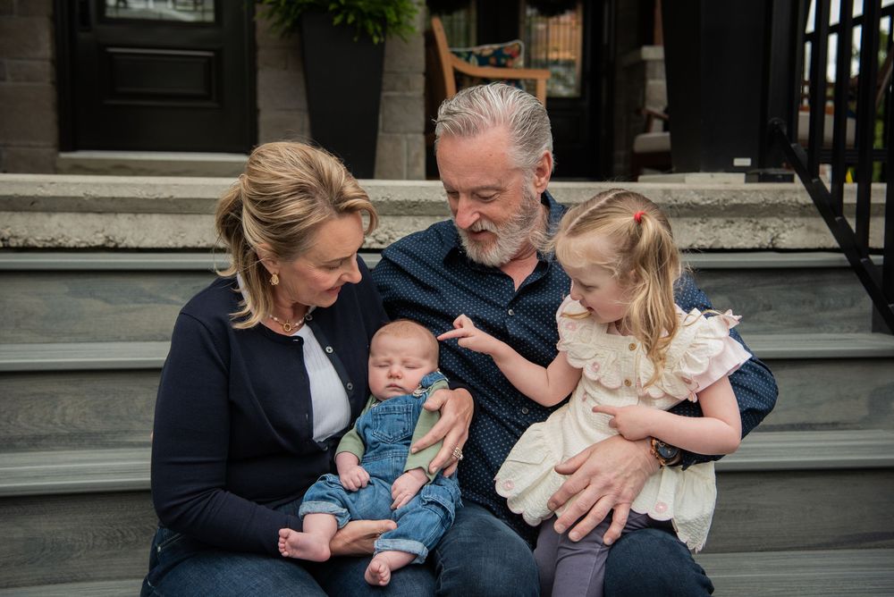 A family gathers on outdoor steps while holding and smiling with their young children.