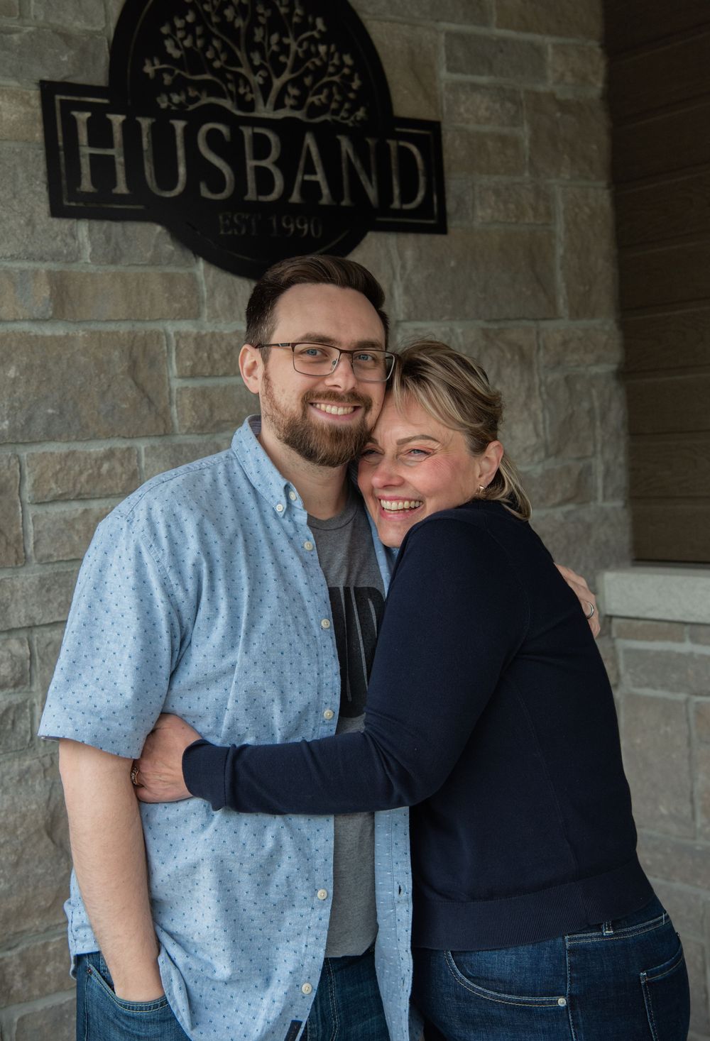 A couple shares a tender embrace while standing on a porch with a stone wall backdrop.