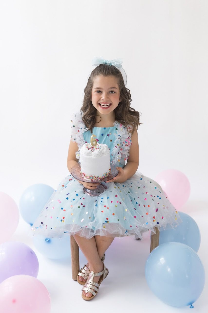 Girl wearing party glasses holding a mini birthday cake with pastel frosting and sprinkles.