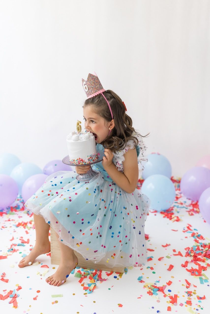 Girl wearing party glasses holding a mini birthday cake with pastel frosting and sprinkles.