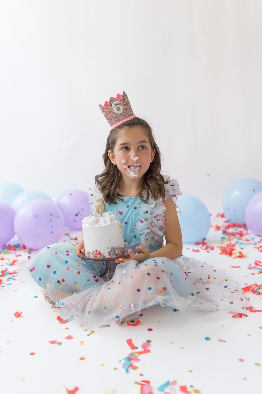 Girl wearing party glasses holding a mini birthday cake with pastel frosting and sprinkles.