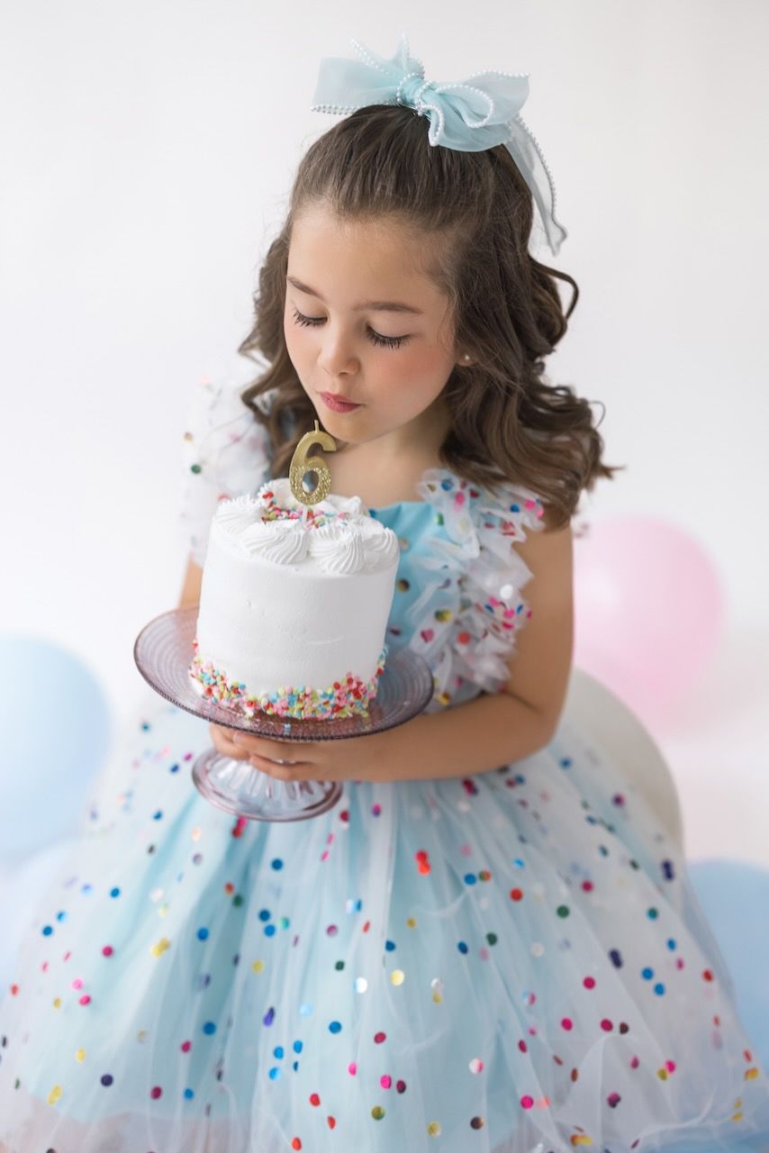 Girl wearing party glasses holding a mini birthday cake with pastel frosting and sprinkles.