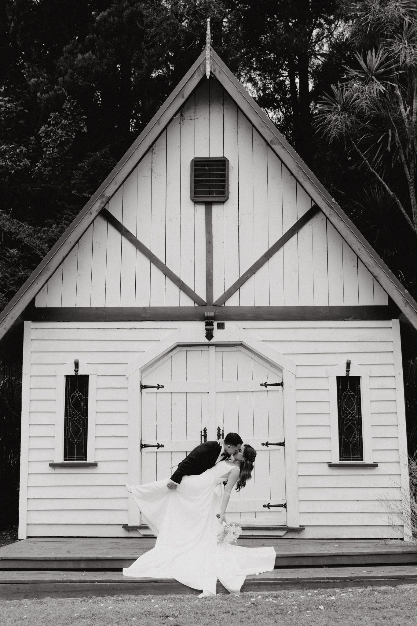 A romantic black and white wedding photo in front of a charming small white chapel captured by Apertured Media Auckland Wedding Photographer