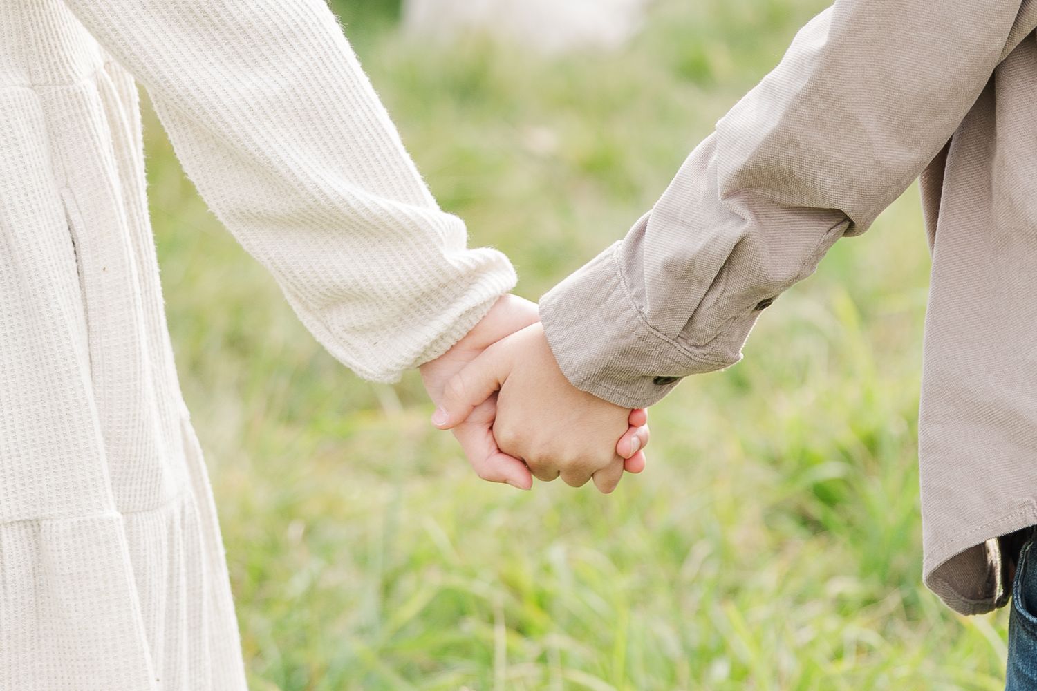 Two people holding hands together against a blurred grass background of green field.