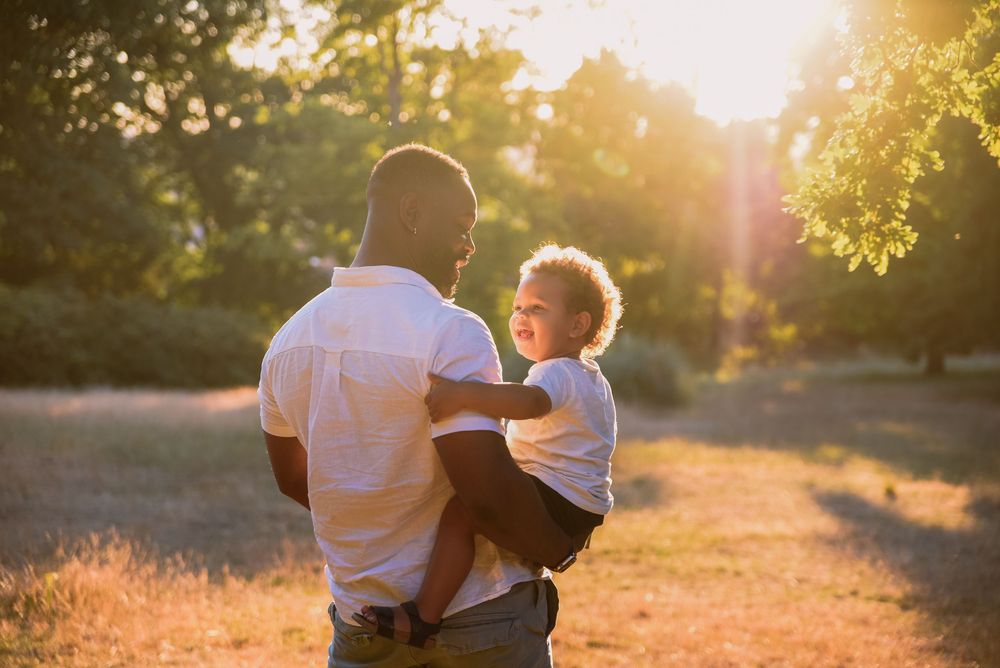 Parent and child sharing tender moment in golden sunlight while standing in nature during sunset.
