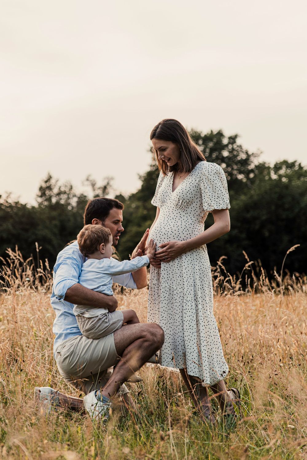 A touching family moment shared in a golden field at sunset as they gather around an expectant mother in a floral dress.