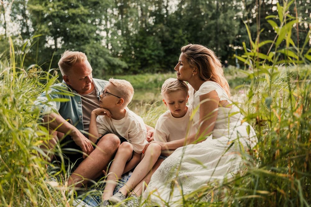 A family sits together in a wildflower field during golden hour, reading and smiling in the summer sunshine.