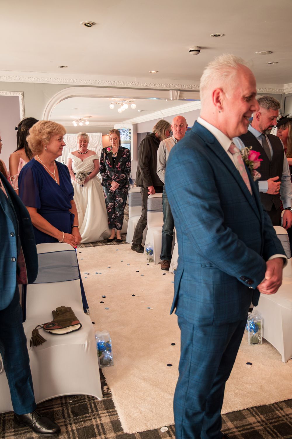 Indoor wedding reception with guests mingling in a room with scattered petals on the floor and recessed lighting above.