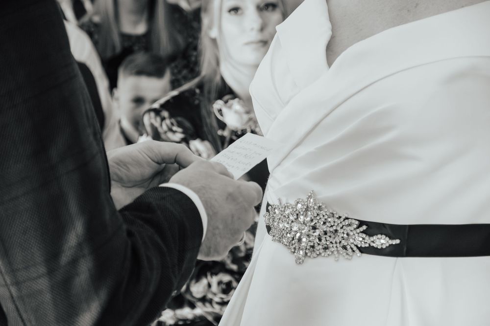 Black and white close-up photo of hands adjusting an ornate crystal sash on a white wedding dress.