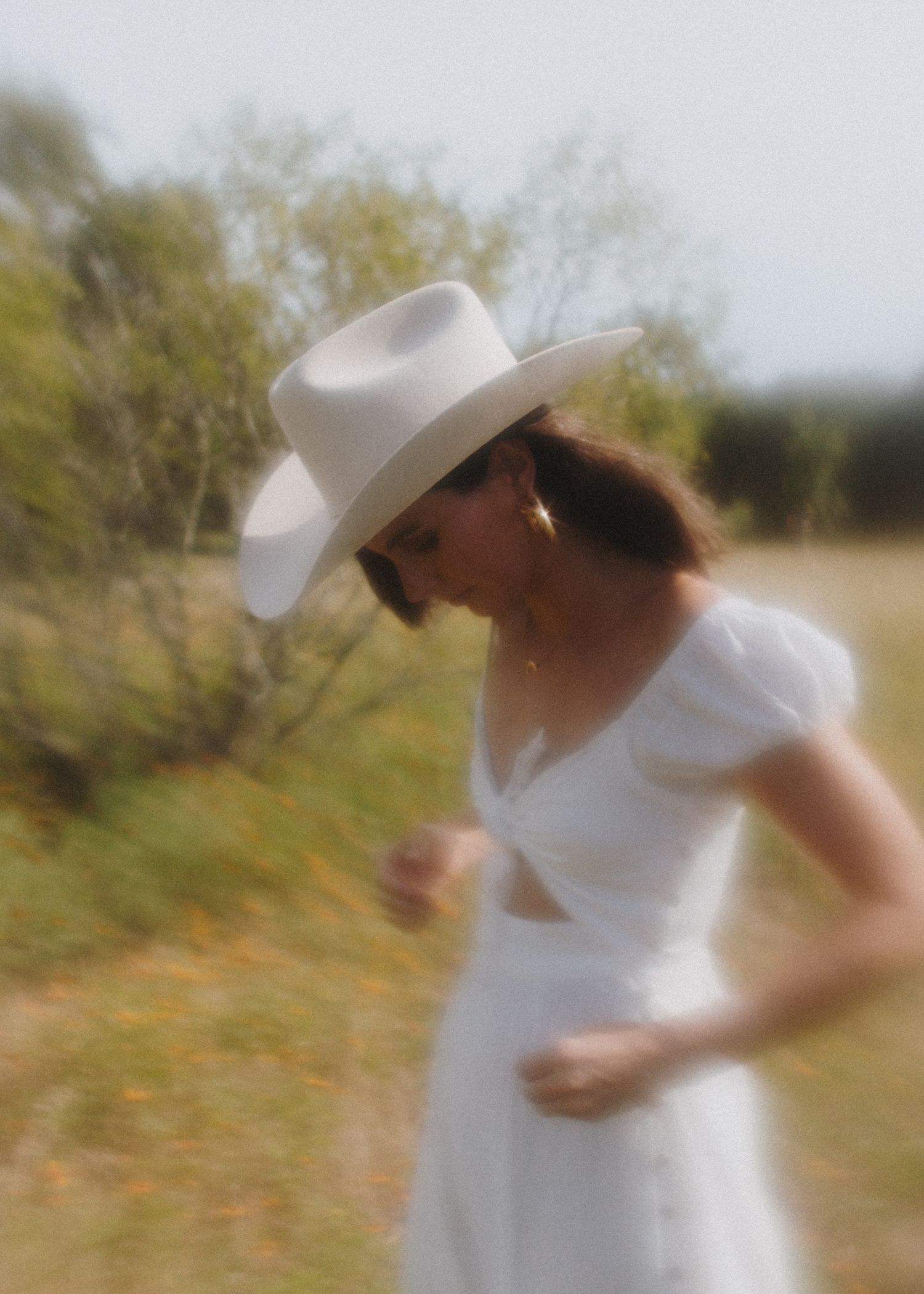 Dreamy vintage-style portrait of woman in white dress and cowboy hat in nature.