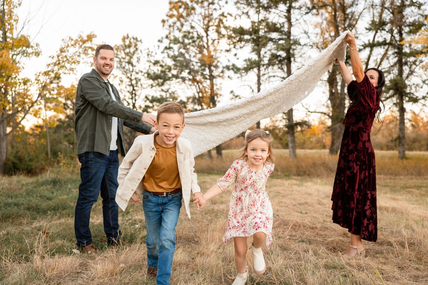 A family plays together outdoors with white fabric in an autumn field during golden hour sunset.