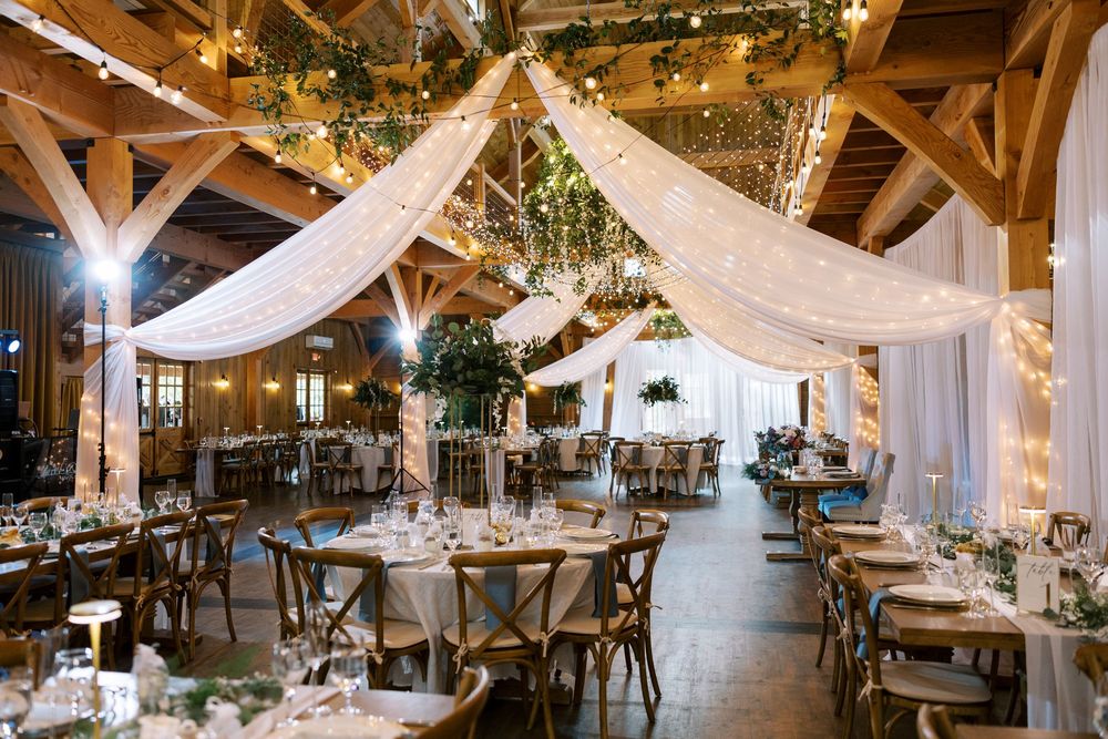 Wedding reception venue at Windham Manor with cathedral ceiling, hanging greenery, string lights and white draping over dining tables.