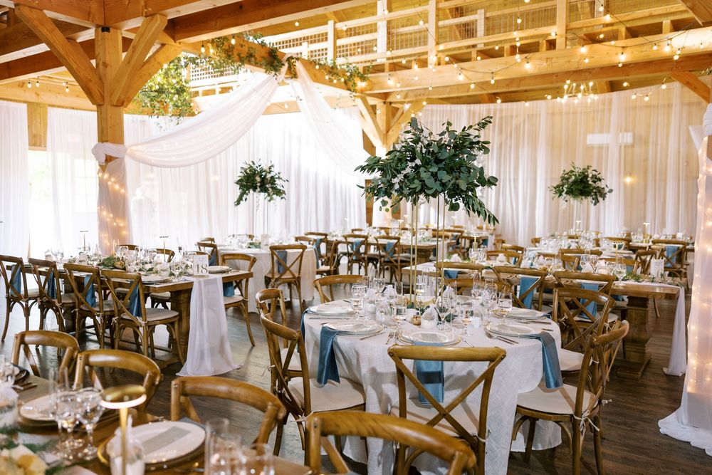 Elegant rustic barn wedding reception setup with wooden crossback chairs and white linens under vaulted wooden beams at Windham Manor.