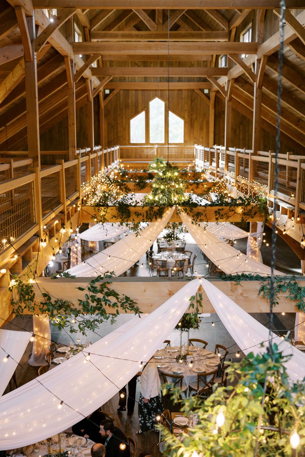 Wedding reception venue at Windham Manor with cathedral ceiling, hanging greenery, string lights and white draping over dining tables.