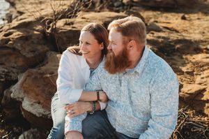 A sweet couple sharing a tender moment while sitting together on rocks during a sunny outdoor photo session.