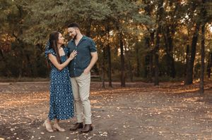 A couple embraces on a sunset-lit forest path, with the person wearing a blue polka dot dress and another in casual attire.