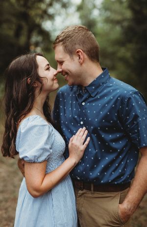 A couple shares an intimate moment outdoors wearing blue and khaki clothing while smiling at each other.