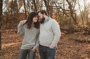 A couple in cozy sweaters sharing an intimate moment together in an autumn forest setting with fallen leaves.