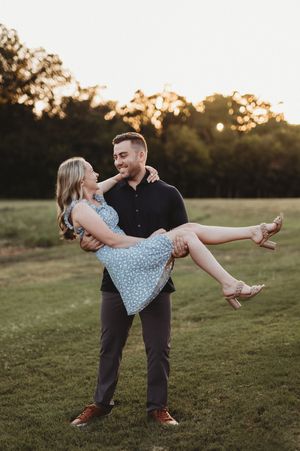 A couple shares a romantic moment at sunset in a grassy field as they pose for an engagement-style photo.