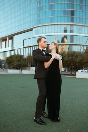 A couple in formal attire dancing elegantly in front of a modern glass building during golden hour.