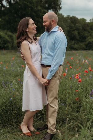 A couple shares a tender moment together in a wildflower meadow with red poppies and blue flowers blooming.
